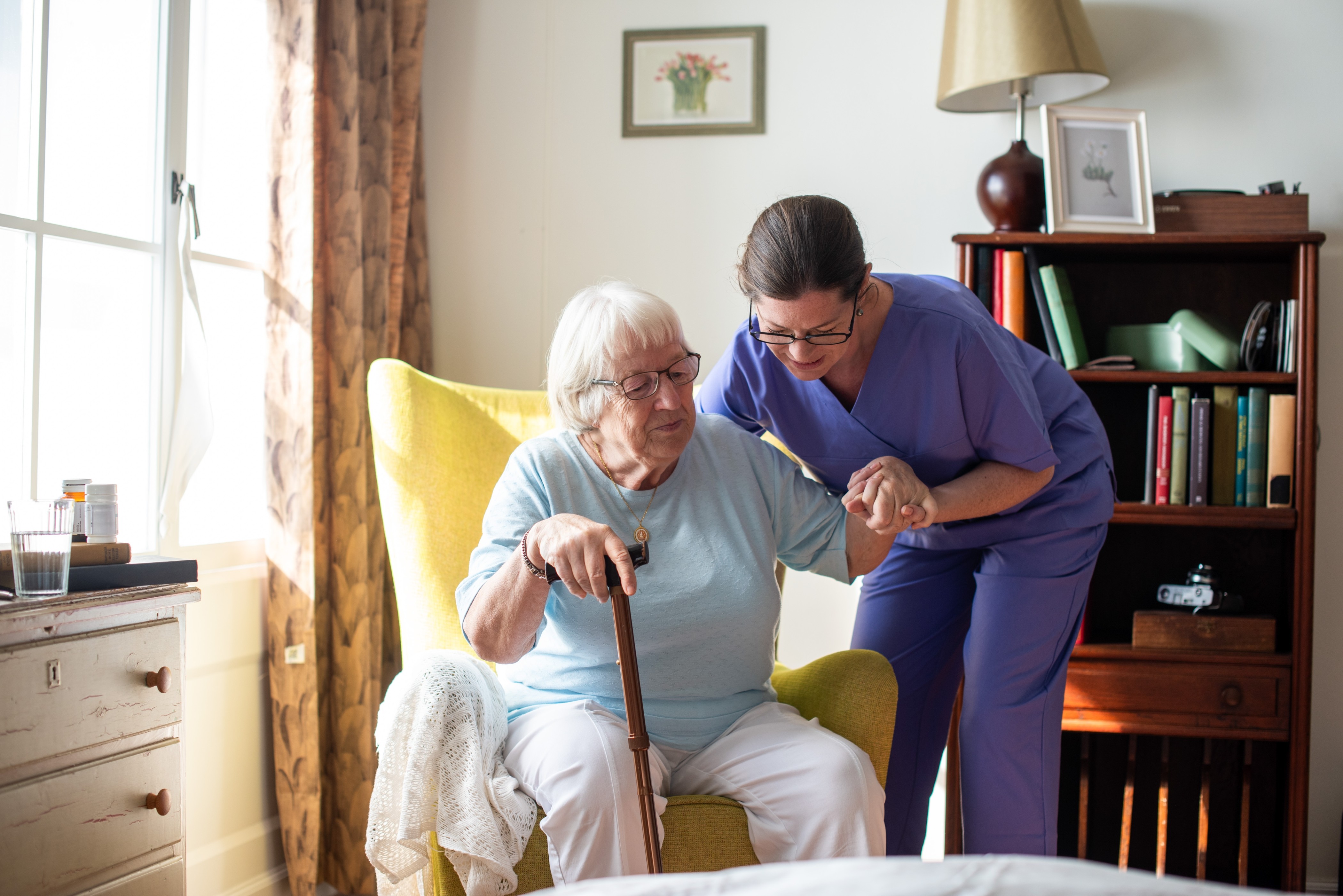 Nurse helping an older woman stand from a chair at home